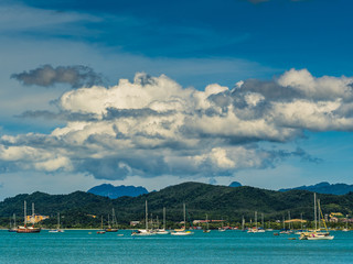 Fototapeta na wymiar View over a busy harbour with lots of sailing boats, mountains in the background and huge fluffy clouds above