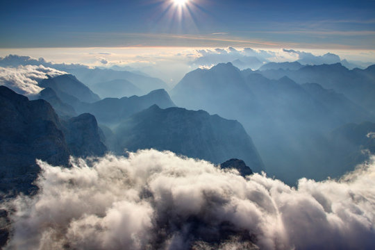 View from Triglav summit with blue ridges of Julian Alps, hazy Trenta valley of Soca river and low white clouds under glowing horizon in autumn sunshine, Triglav National Park Slovenia / Italy Europe