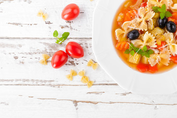 Minestrone, vegetarian soup with pasta and vegetables on white wooden rustic background. Traditional italian food. Top view