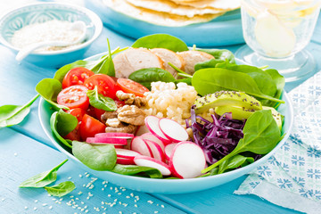 Bowl with grilled chicken meat, bulgur  and fresh vegetable salad of radish, tomatoes, avocado, kale and spinach leaves. Healthy and delicious summer lunch