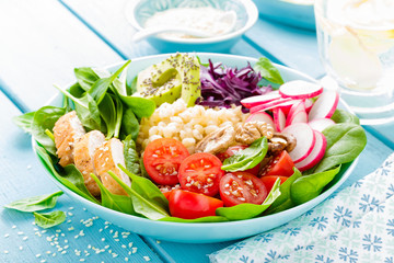 Bowl with grilled chicken meat, bulgur  and fresh vegetable salad of radish, tomatoes, avocado, kale and spinach leaves. Healthy and delicious summer lunch