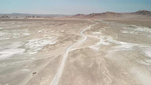 Aerial landing footage of a desert that has a Mars like landscape with brown hills and a dirt road