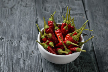 Chilli pods in a white bowl on a black wooden rustic table. The view from the top.