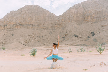 Young woman doing yoga in desert with mountains at sunrise time