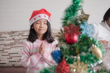 Asian little girl with mother praying near a christmas tree for party with happiness