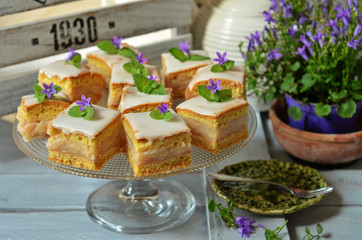 Square pieces of apple pie with icing on a glass plateau on a wooden background