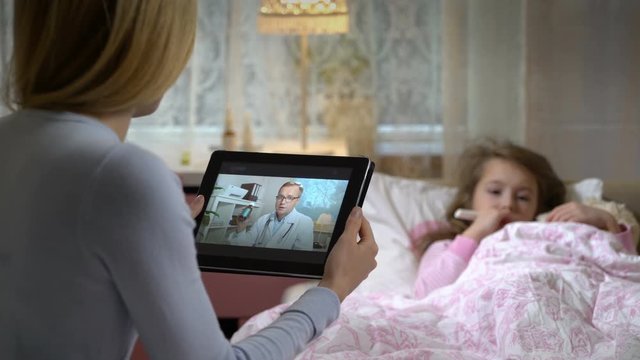 Medicine online. Home quarantine coronavirus. Mom with a little sick daughter gets a doctor's advice using video chat at home. Male doctor prescribing her medicine.