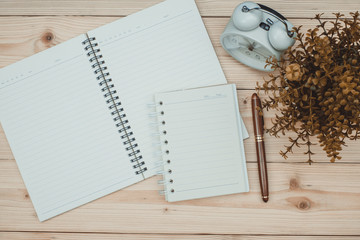 Office supplies or office work essential tools items on wooden desk in workplace, pen with notebook and alarm clock, top view