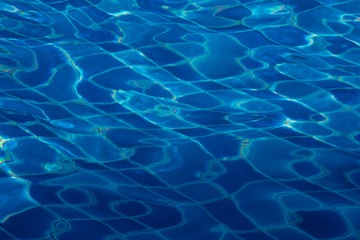 Blue and bright ripple water surface in swimming pool with sun reflection.