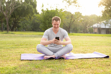 Young happy man smiling while using phone at the park