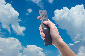 hand holds tv remote against the blue sky with white clouds. 4k television.