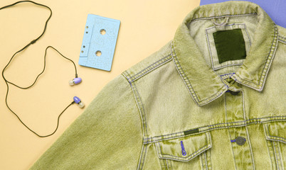 Yellow jeans jacket, audio cassette, vacuum earphones on colored background. Retro media, music lover, 80s. Top view, flat lay.