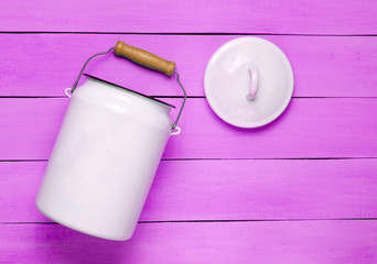 Enameled milk can on violet wooden background. Top View.