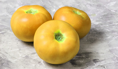 Three yellow ripe tomatoes on a gray concrete background..