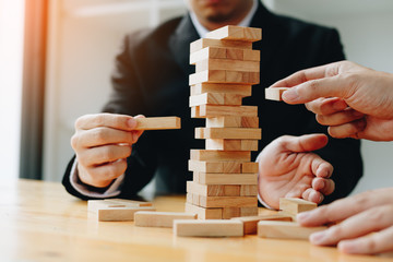 Two businessmen help to hold the wood block to fall down.