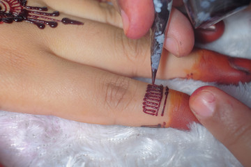 Image detail of henna being applied to hand over white fabric. Selective focus.