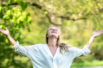 Euphoric woman smiling and laughing with her hands raised outdoors in nature