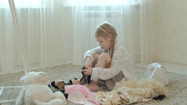 cheerful girl with pigtails in a pink skirt tries on adult mother's clothes, dresses, high heels and dances in front of a mirror with a bag, mothers wardrobe