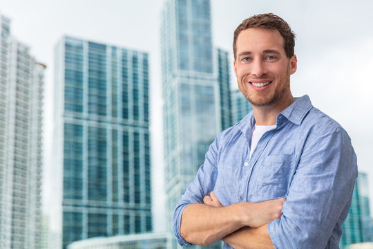 Happy Young Man Businessman Portrait Young Smiling Confident In Front Of Modern Condo Building Skyscraper Outside. City Lifestyle People.