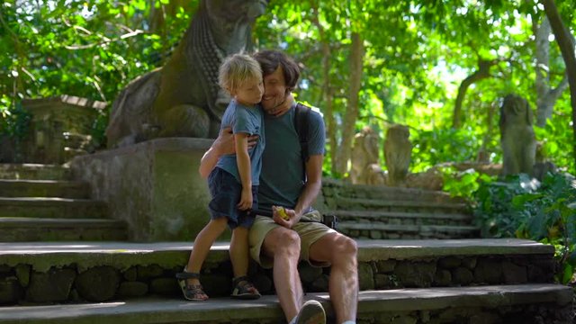 Slow motion shot of a young man and his little son sitting on the stairs in the Monkeys forest eco-park in Ubud, Indonesia