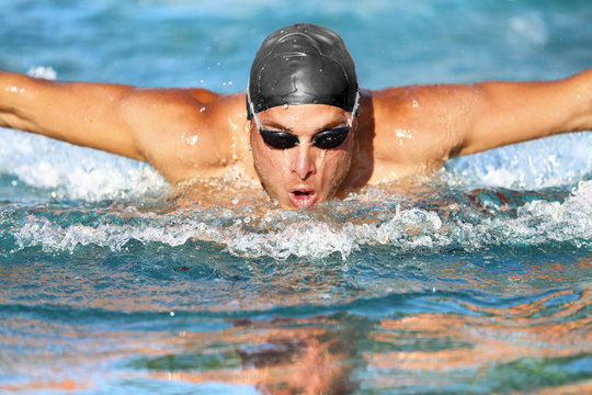 Swimmer. Man swimming butterfly strokes in pool competition. Competitive male sport athlete swimmer wearing swimming goggles and cap. Young caucasian fitness model face portrait.