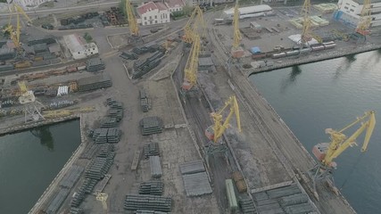 Aerial of Odessa business seaport with stockpiled barrels, cranes and containers