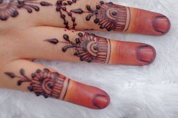 Image detail of henna being applied to hand over white fabric. Selective focus.