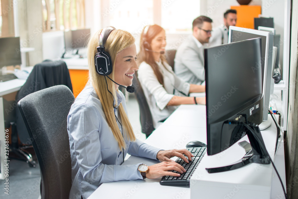 Wall mural Smiling agent woman with headsets helping a customer accompanied with her team in call center