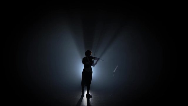 Woman plays the violin and looks at the music stand in the dark . Silhouette. Black smoke background