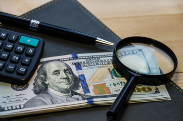 dollar, notepad, pen, calculator and magnifier on a wooden table