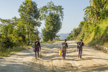 schoolchildren girl and boys go to school on a dirt road in the forest against the backdrop of the mountains