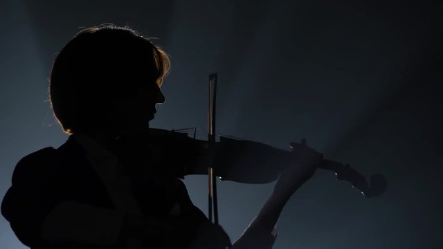 Violinist performing in a dark studio with a lantern. Black background. Silhouette