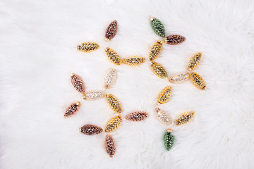 Frame in form of snowflake made from  decorative golden, brown  and silver pine cones on white  fur background.