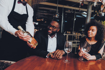 Obraz premium African Couple Offerring Bottle Wine in Restaurant