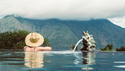 Relax and spa concept. Woman with a hat relaxing in a pool towards the mountain in Bali