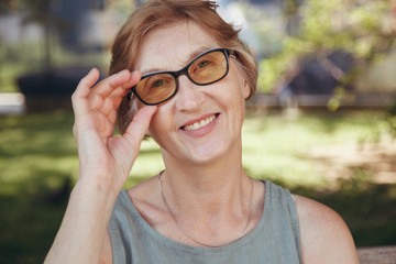 The happy woman the pensioner wearing spectacles has a rest in the park and smiles