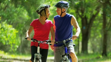 Happy fit Caucasian American seniors enjoying bike ride to keep fit outdoors in the park 
