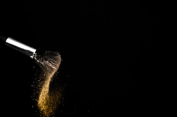 golden powder splash and brush for makeup artist or beauty blogger in black background