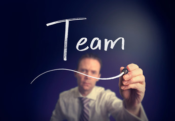 A businessman writing a Team concept with a white pen on a clear screen.