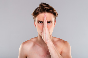 This is a part of me. Portrait of handsome shirtless young man cowering his face with his hand and...