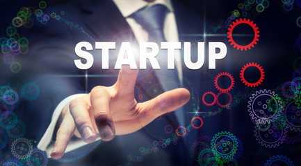 A businessman pressing a Startup business concept on a graphical display of cogs