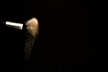 golden powder splash and brush for makeup artist or beauty blogger in black background