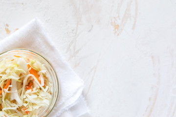 Top view glass jar with sauerkraut on white towel on white background.