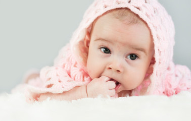 Portrait of a crawling beautiful bright baby in the hood on the bed in his room. Suck a hand.