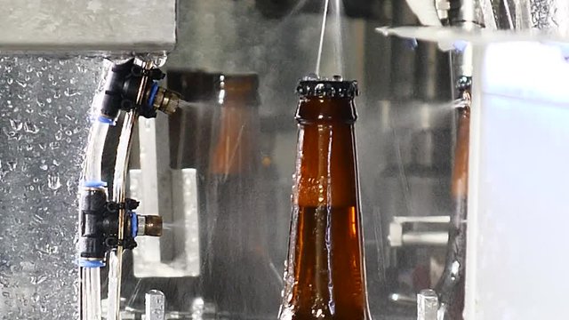 Brewery concept. Beer factory. Automatic Beer Bottling Line. Close up shot of final part of beer bottles production on transporting line. Ready bottles are being washed. 4k