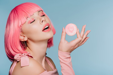 seductive girl in pink wig posing with macaron isolated on blue