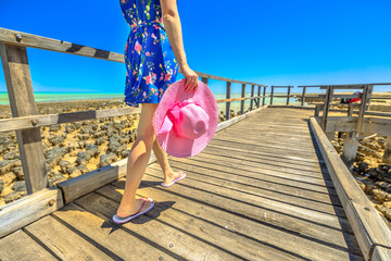 Woman in hat walking on wooden path at Stromatolites Hamelin Pool. Marine Reserve, Shark Bay, Western Australia. following low angle legs in Australian travel destination.
