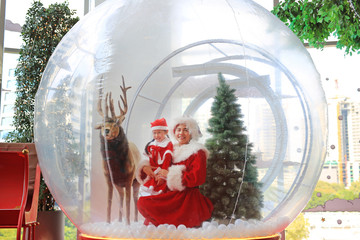 Happy little child girl and mother in santa costume dress has fun in big winter Snow globe with...