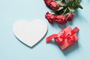 Valentine's card made of white heart for space, giftbox, bouquet red roses on pastel blue background. Copy space.