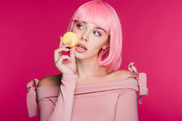 fashionable woman in pink wig posing with macaron isolated on pink